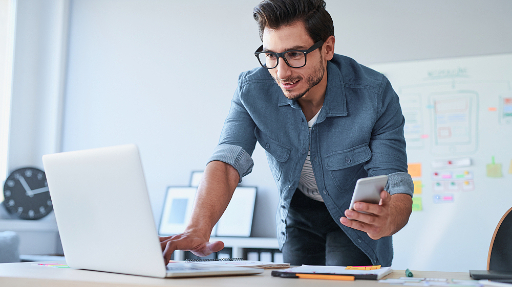 Datensicherung auf deutschen Backup-Servern Mann hält Handy in der Hand und arbeitet am Laptop