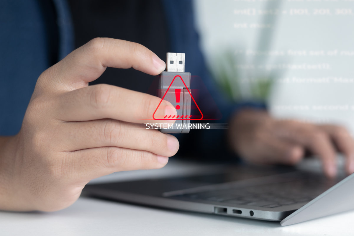 USB-Stick mit Warnsignal in der Hand einer Person vor einem Laptop